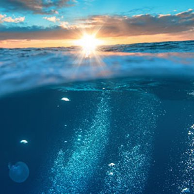 View of the ocean and sky, with the sun beaming in the centre of screen and emitting rays of golden light